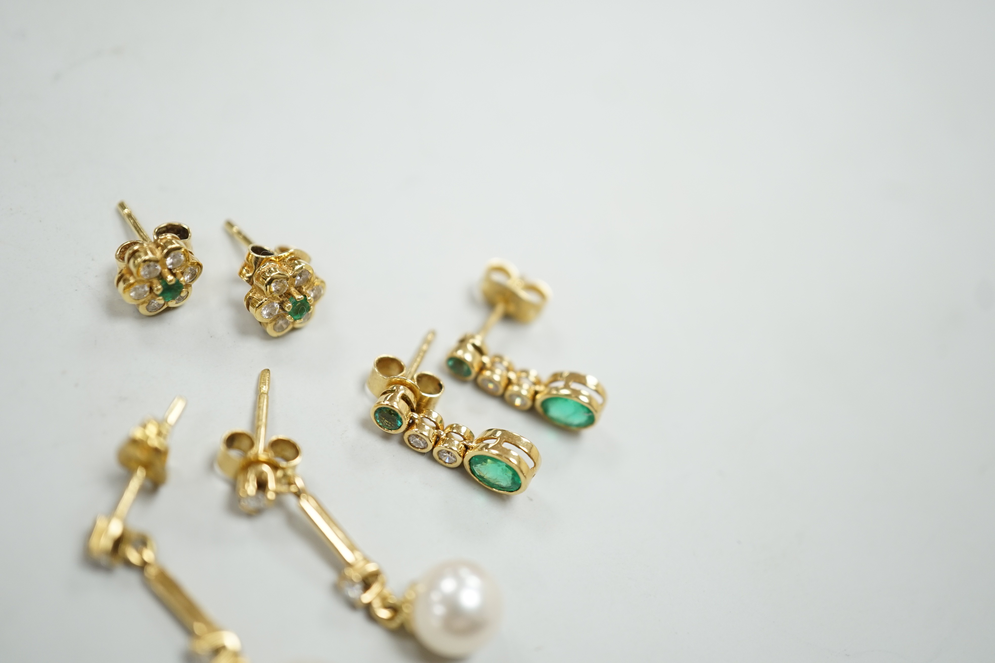 Two modern pairs of 18ct gold, emerald and diamond set ear studs and a pair of 18ct gold, cultured pearl and diamond set ear studs, gross weight 7 grams.